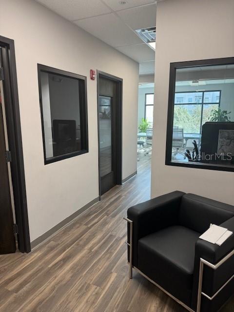 A hallway with wood-look flooring leads past office doors to a room with large windows — 13550 VILLAGE PARK DRIVE UNIT GE, ORLANDO, FL