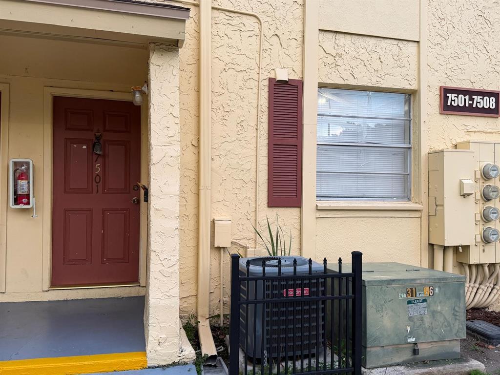 An exterior view of a building entrance with a red door, window, and utility equipment — 7501 GALLINETA COURT, TAMPA, FL