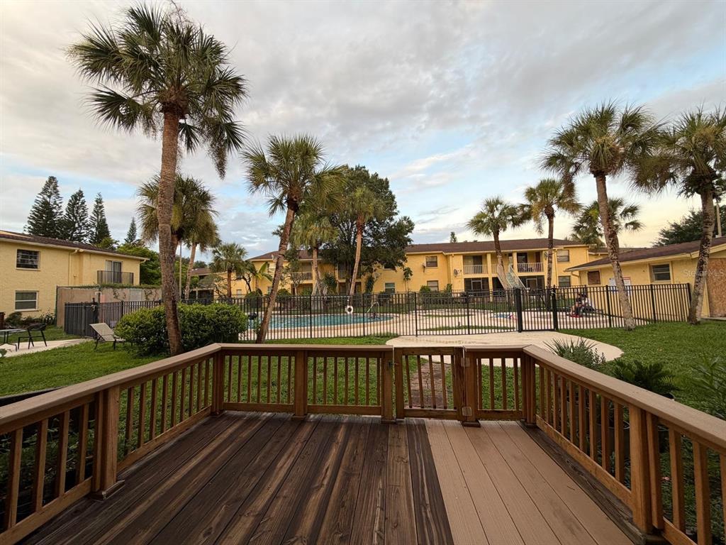 A wooden deck overlooks a fenced-in swimming pool surrounded by palm trees and apartment buildings — 7501 GALLINETA COURT, TAMPA, FL