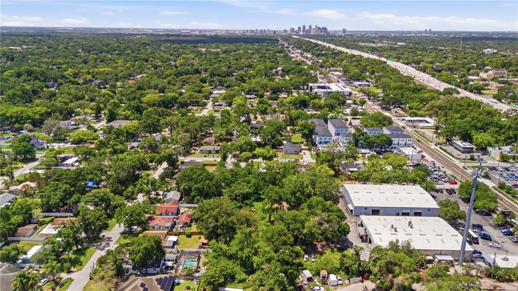 An aerial view shows a residential neighborhood with trees, commercial buildings, and a distant city skyline — 6612 N 9TH STREET, TAMPA, FL