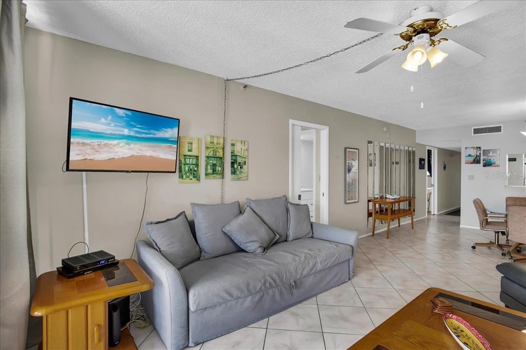A living room features a gray sofa, a wall-mounted television, and tile flooring — 15462 GULF BOULEVARD UNIT 903, MADEIRA BEACH, FL