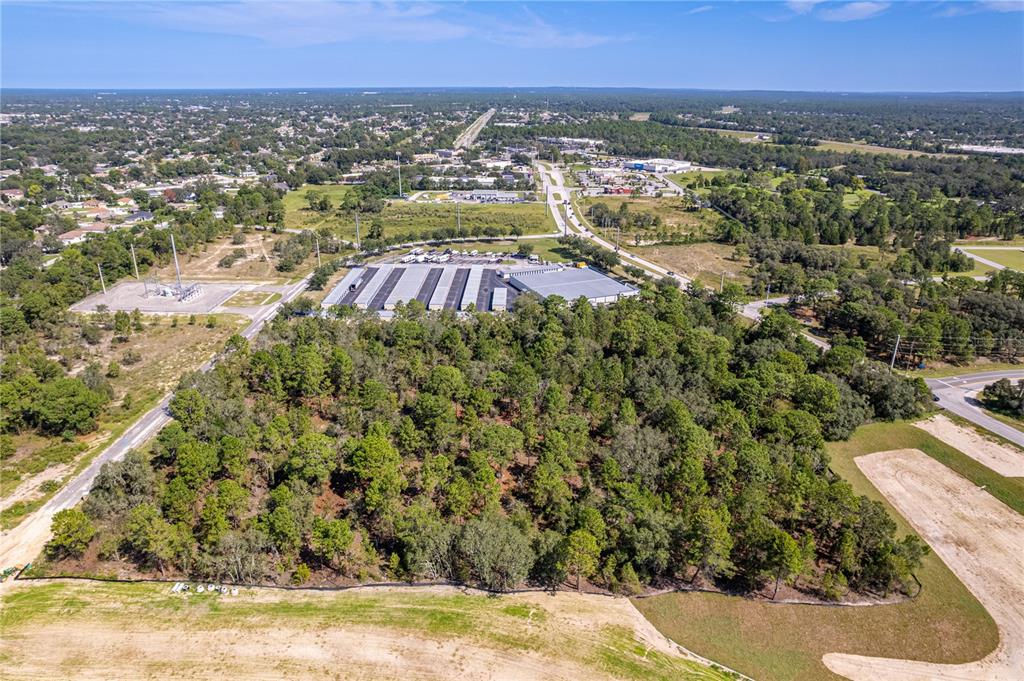 An aerial view shows a wooded lot adjacent to a commercial building and parking area — 0 ANDERSON SNOW ROAD, SPRING HILL, FL