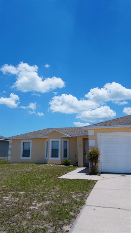 A single-story house with a yellow stucco exterior, a white garage door, and a driveway — 1417 SARASOTA DRIVE, KISSIMMEE, FL