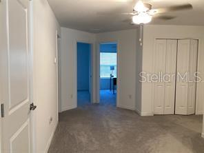 A carpeted room features a ceiling fan, white walls, and two doorways leading to other rooms — 17522 NECTAR FLUME DRIVE, LAND O LAKES, FL
