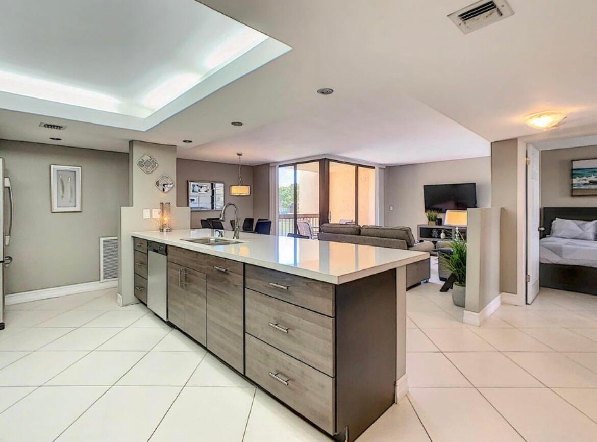 A modern kitchen with wood-toned cabinets and white countertops opens into a living area — 2455 Lindell Boulevard # 3203, Delray Beach FL 33444, DELRAY BEACH, FL