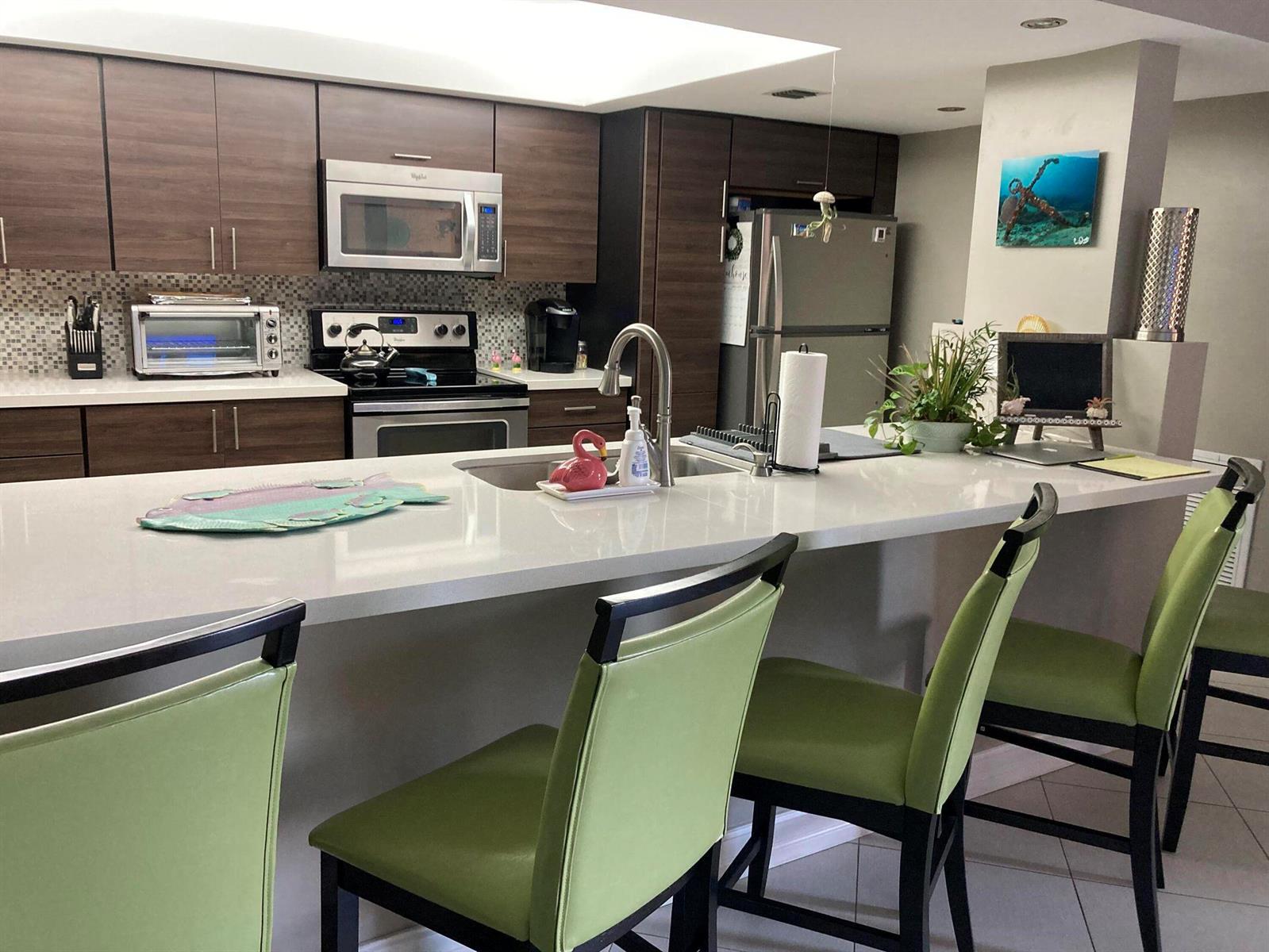 A kitchen features dark wood cabinets, a white quartz island, and green bar stools — 2455 Lindell Boulevard # 3203, Delray Beach FL 33444, DELRAY BEACH, FL