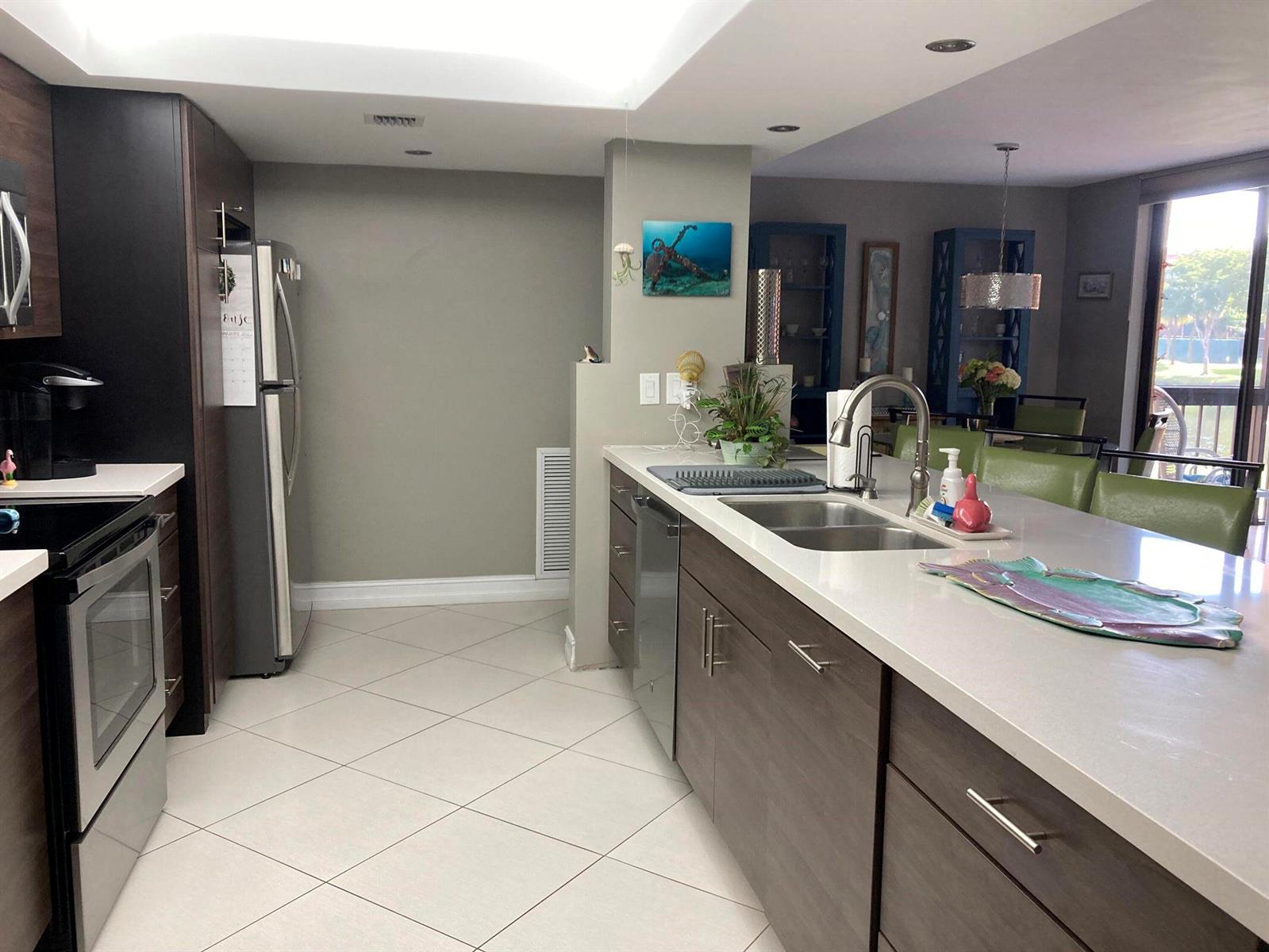 A modern kitchen features dark wood cabinetry, white countertops, stainless steel appliances, and tile flooring — 2455 Lindell Boulevard # 3203, Delray Beach FL 33444, DELRAY BEACH, FL