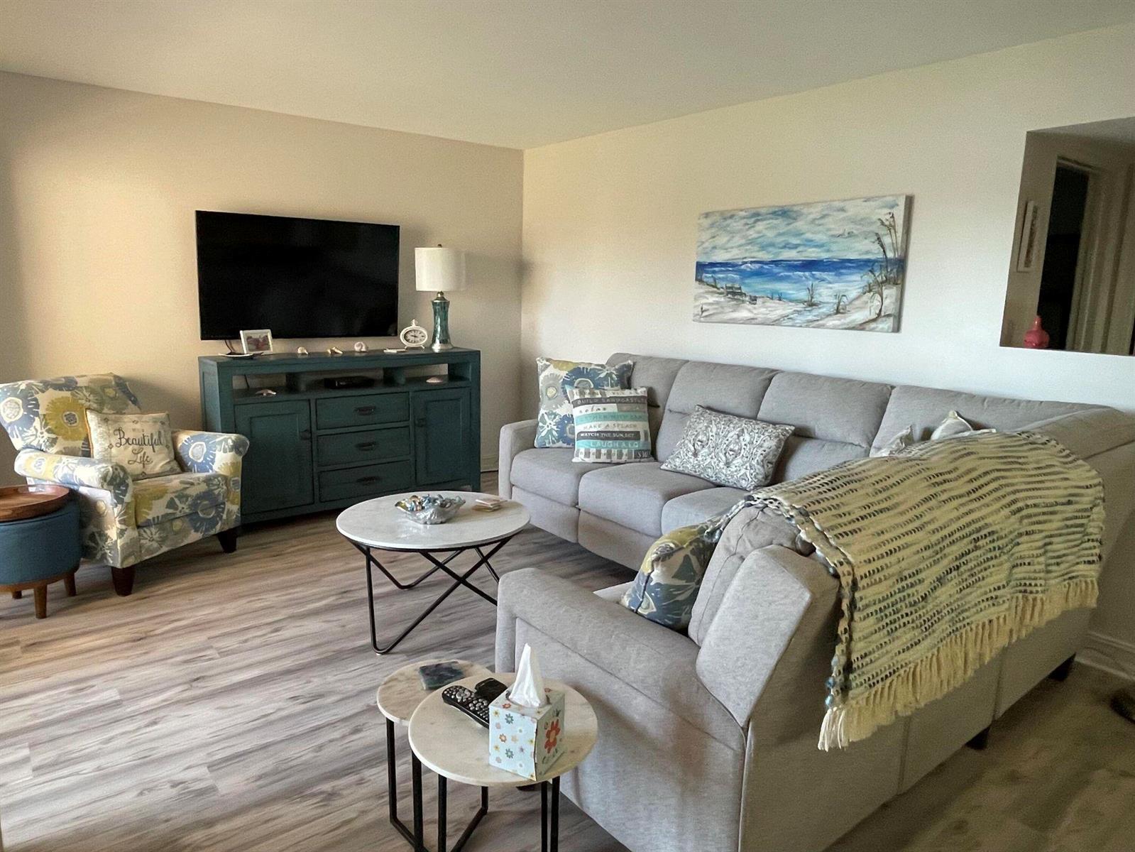 A living room features a grey sectional sofa, a patterned armchair, and a teal media console — 2455 Lindell Boulevard # 3203, Delray Beach FL 33444, DELRAY BEACH, FL