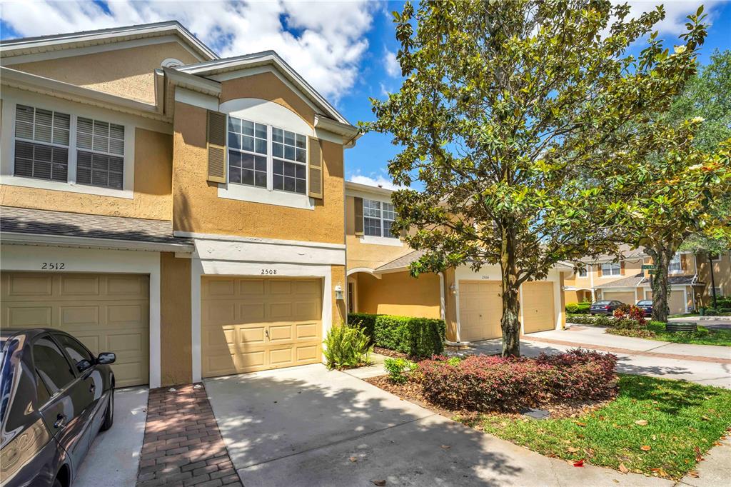 A two-story townhouse exterior features tan stucco walls, a brick driveway, and a large tree — 2508 GALLIANO CIRCLE, WINTER PARK, FL