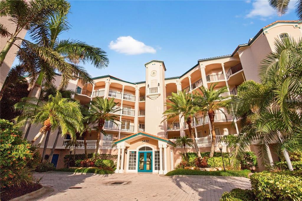 A multi-story beige apartment building with arched balconies and a central entrance under palm trees — 5430 EAGLES POINT CIRCLE UNIT 202, SARASOTA, FL