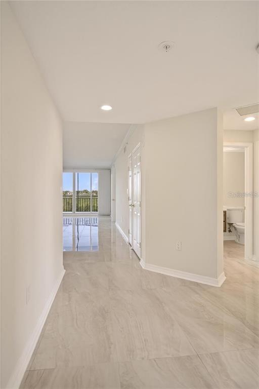 A hallway with light-colored tile flooring leads toward a windowed living area and bathroom — 5430 EAGLES POINT CIRCLE UNIT 202, SARASOTA, FL