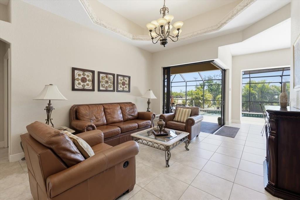 A living room with leather furniture, a glass coffee table, and sliding doors to a pool — 19 MEDALIST WAY, ROTONDA WEST, FL