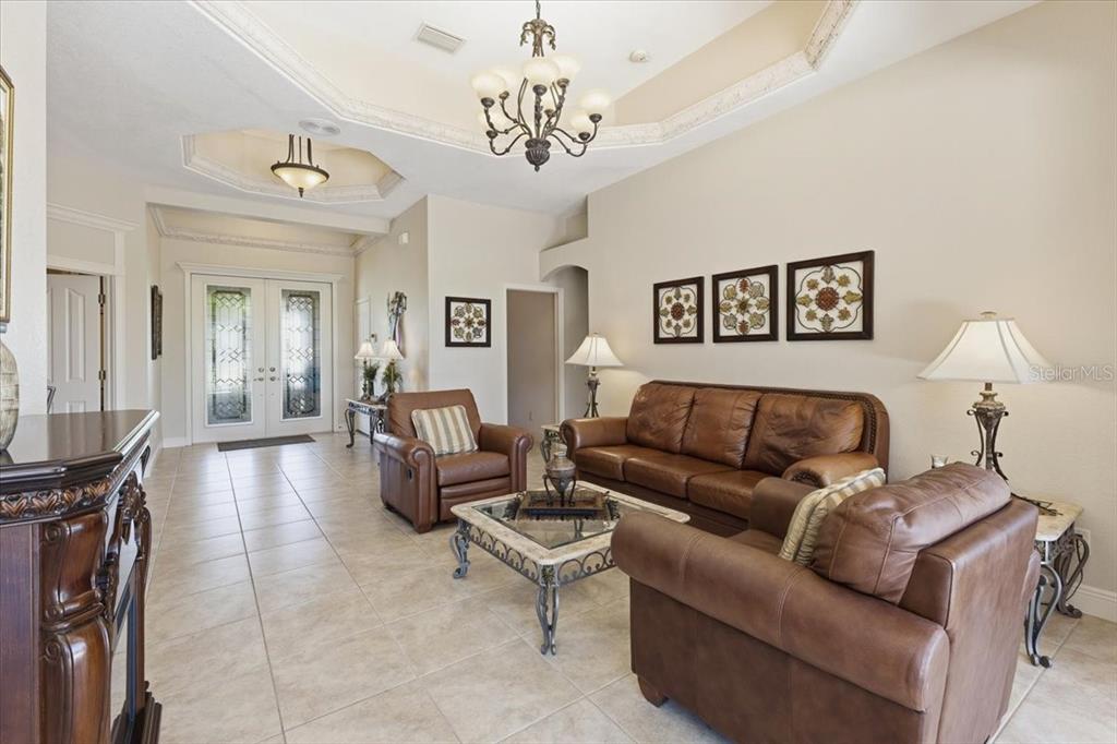 A living room features tile floors, leather furniture, a chandelier, and a tray ceiling — 19 MEDALIST WAY, ROTONDA WEST, FL