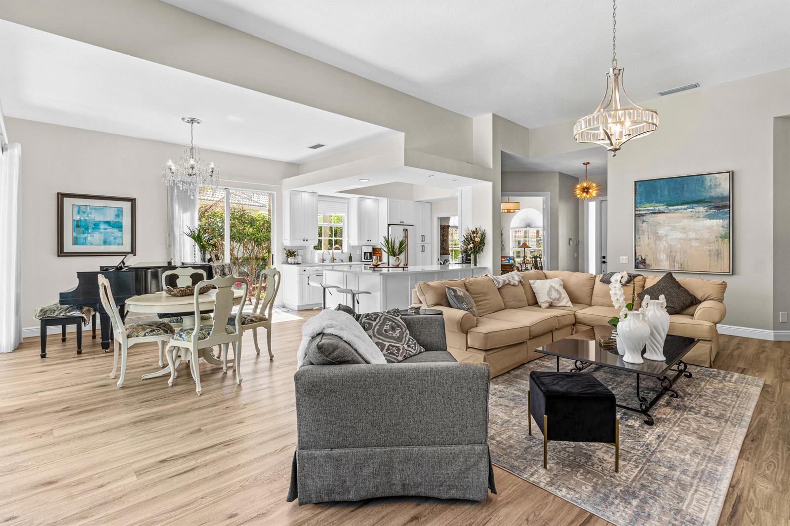 An open-concept living and dining area features a grand piano, white kitchen, and neutral furnishings — 4983 Garden Drive, Delray Beach FL 33445, DELRAY BEACH, FL
