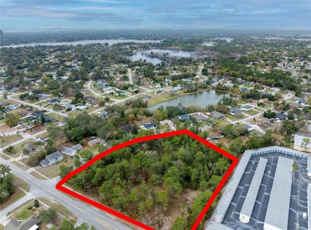 An aerial view shows a wooded, rectangular vacant lot outlined in red next to buildings — 1370 COURTLAND BLVD, DELTONA, FL