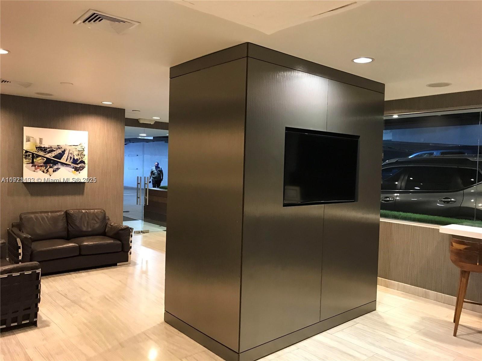 A modern lobby features a dark central partition with a mounted television and leather seating — 150 SE 2nd Ave, Miami FL 33131, MIAMI, FL