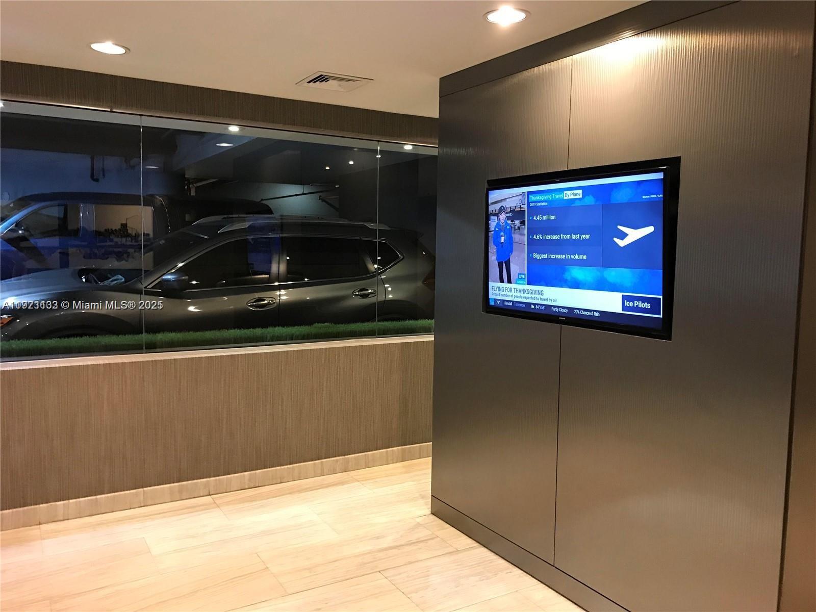 A modern lobby features a wall-mounted television and a large glass window overlooking a garage — 150 SE 2nd Ave, Miami FL 33131, MIAMI, FL