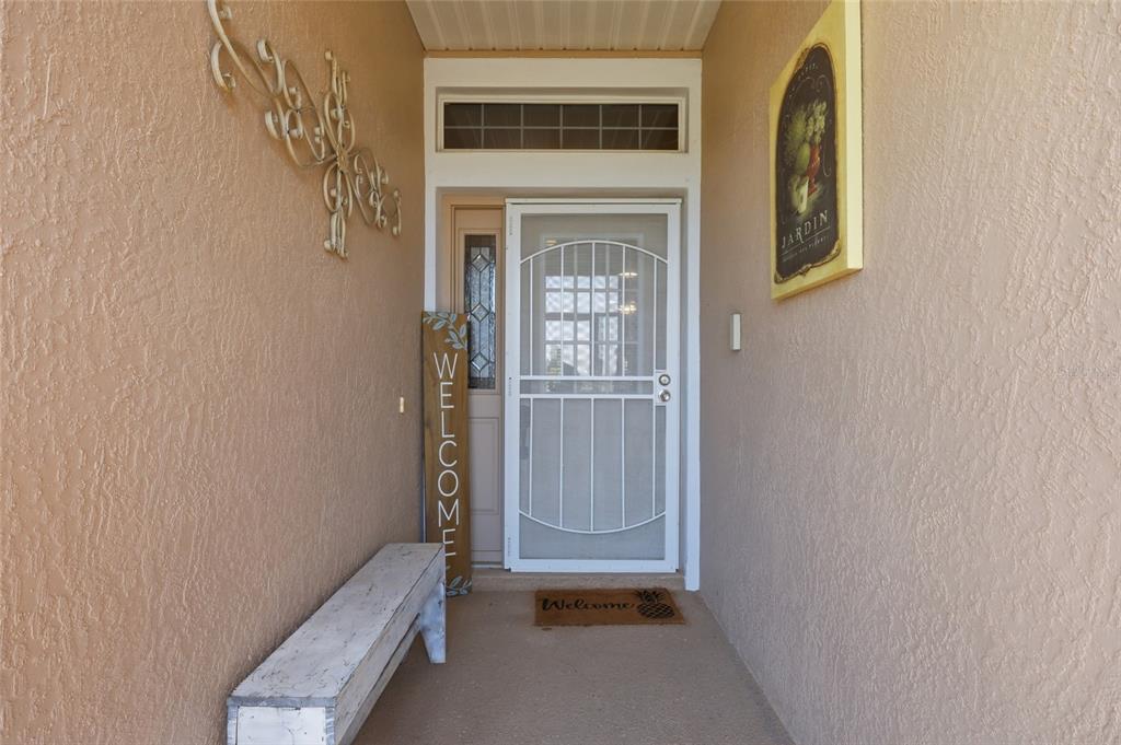 A covered entryway features a white storm door, a wooden bench, and decorative wall art — 6342 SANDERS GROVE CIRCLE, OKAHUMPKA, FL