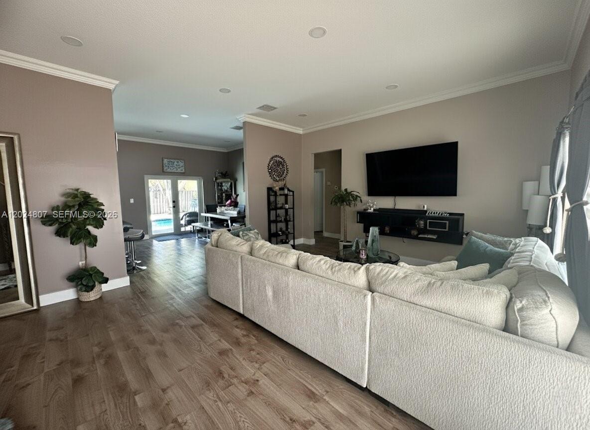 A living room features a large sectional sofa, wood-look flooring, and a wall-mounted television — 14127 SW 161st Pl, Miami FL 33196, MIAMI, FL