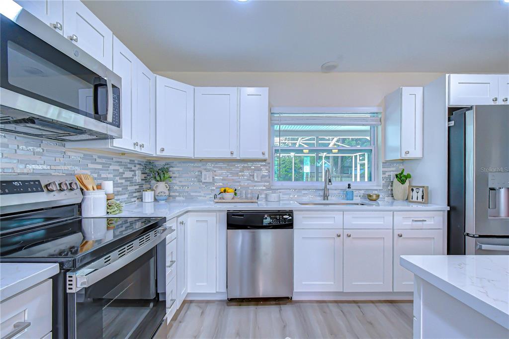 A kitchen features white cabinets, stainless steel appliances, a tiled backsplash, and light-colored flooring — 2167 LAKEVIEW ROAD, CLEARWATER, FL