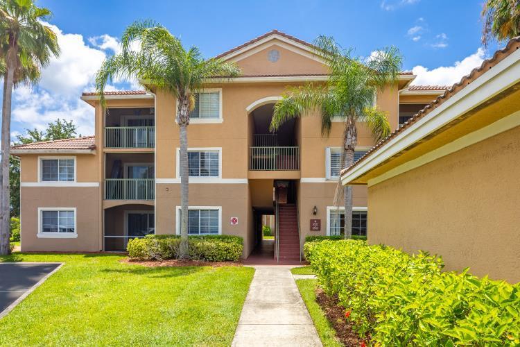 A three-story apartment building with tan stucco walls, balconies, and palm trees on a lawn — 3721 NW Mediterranean Lane # 304, Jensen Beach FL 34957, JENSEN BEACH, FL