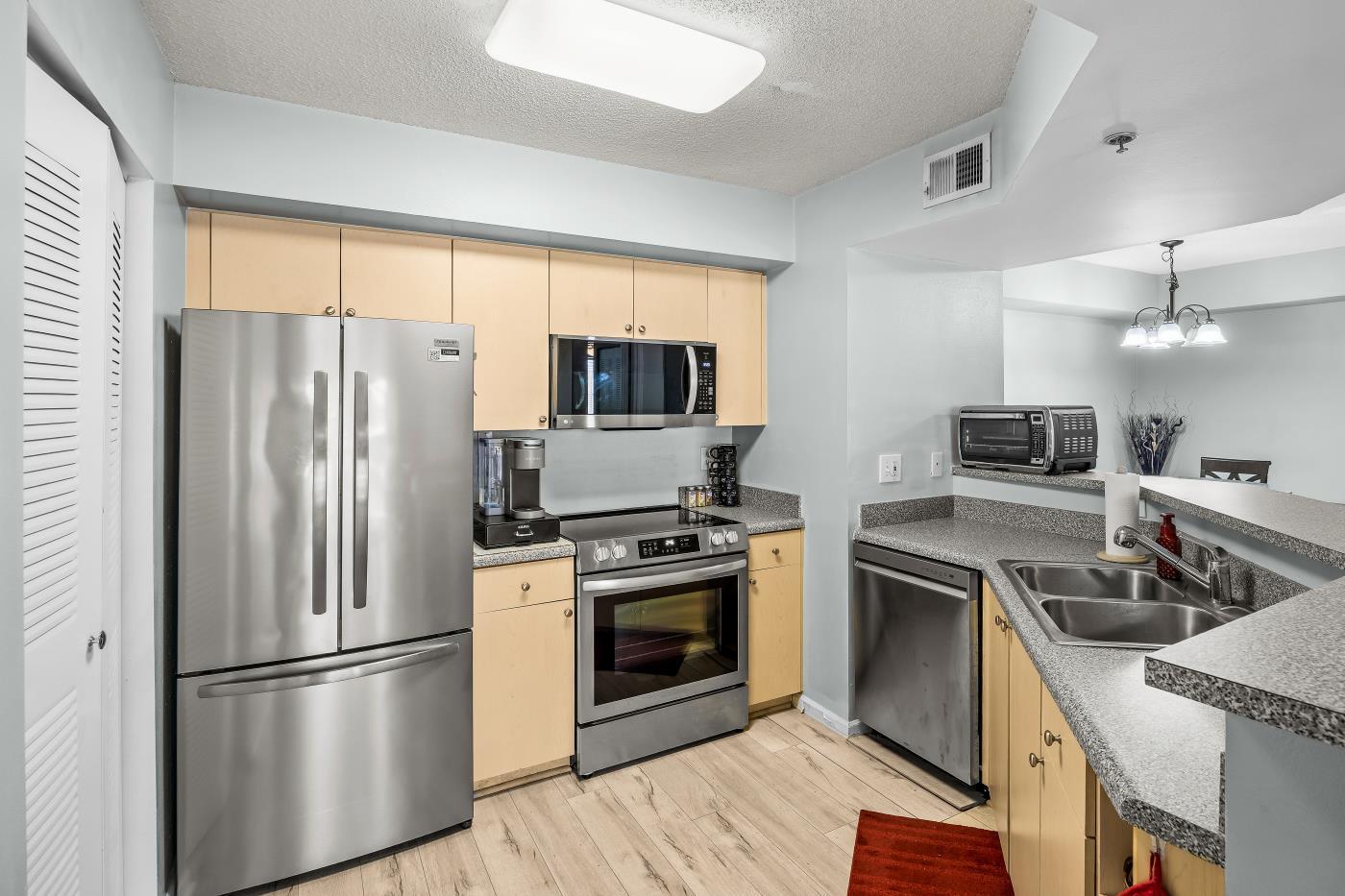 A kitchen features light wood cabinets, stainless steel appliances, grey countertops, and light wood flooring — 3721 NW Mediterranean Lane # 304, Jensen Beach FL 34957, JENSEN BEACH, FL