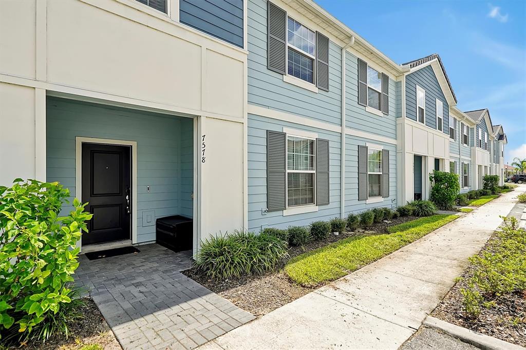 A light blue multi-story townhouse exterior features a black front door and a paved walkway — 7578 OAK SPRING LANE, DAVENPORT, FL