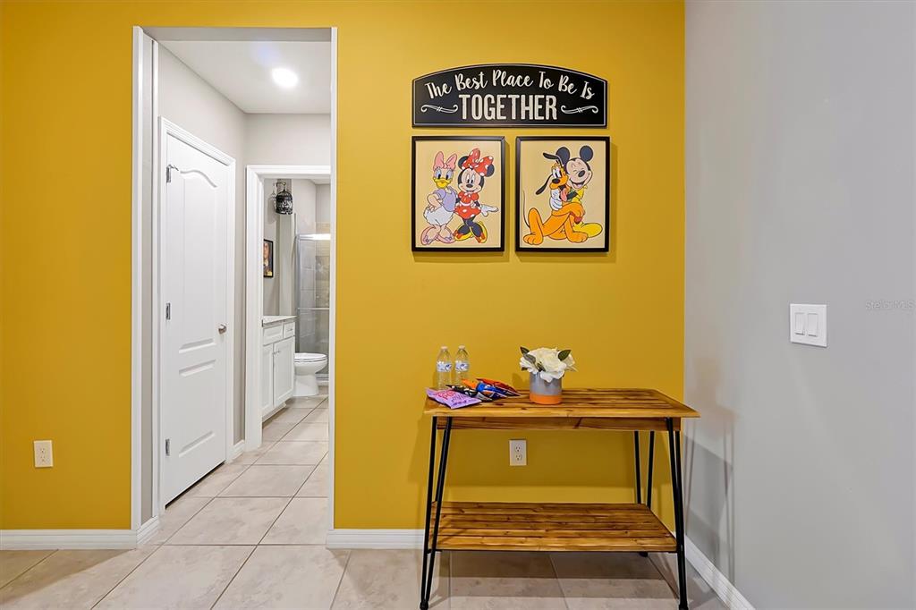 A yellow wall features Disney-themed artwork above a wooden console table in a hallway — 7578 OAK SPRING LANE, DAVENPORT, FL