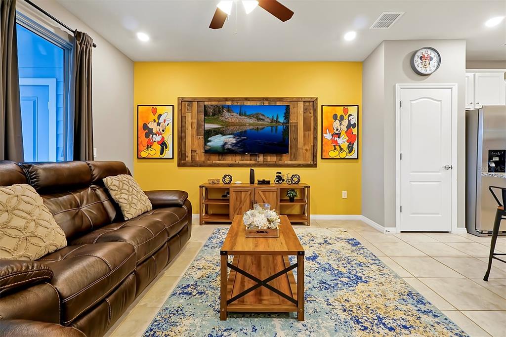 A living room features a yellow accent wall, a mounted television, and a brown sofa — 7578 OAK SPRING LANE, DAVENPORT, FL