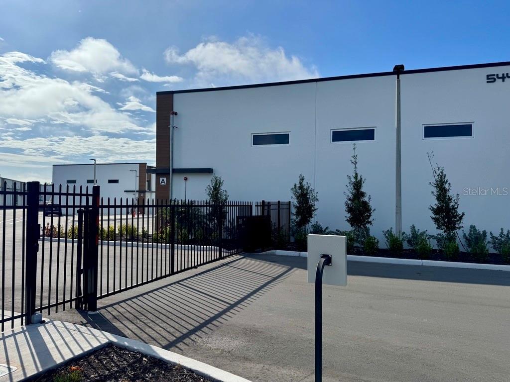 A white industrial building with a black metal fence and gate in the foreground — 5421 COMMUNICATIONS PARKWAY UNIT 40, LAKEWOOD RANCH, FL