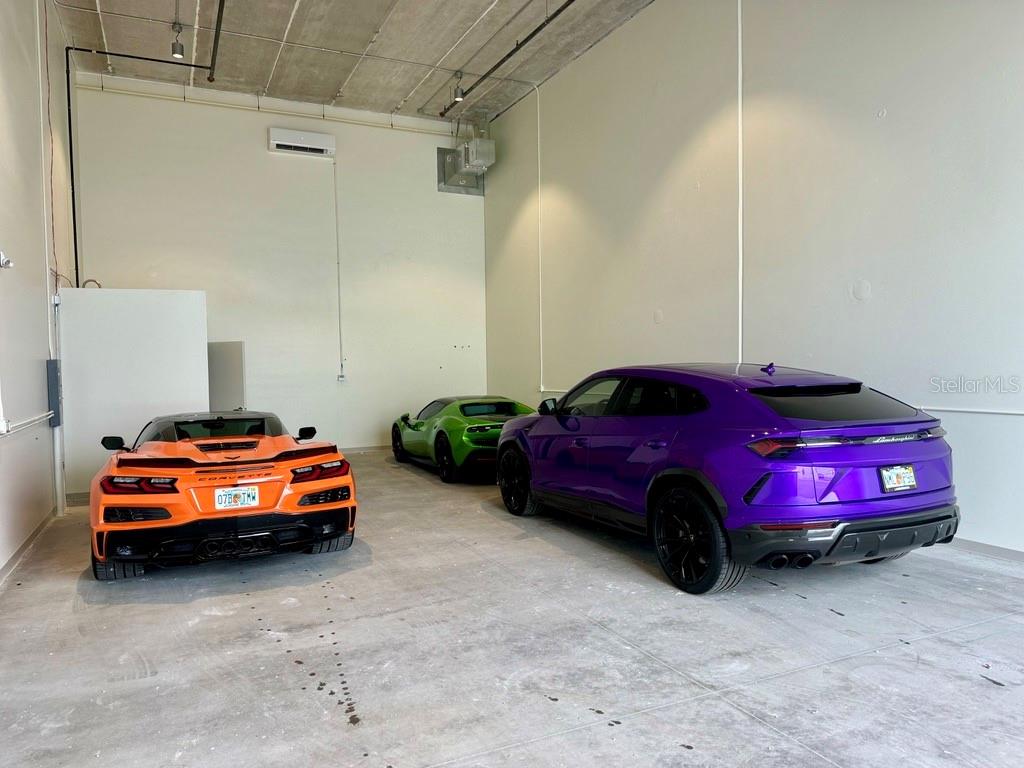 A garage with high ceilings contains an orange Corvette, a green sports car, and a purple SUV — 5421 COMMUNICATIONS PARKWAY UNIT 40, LAKEWOOD RANCH, FL