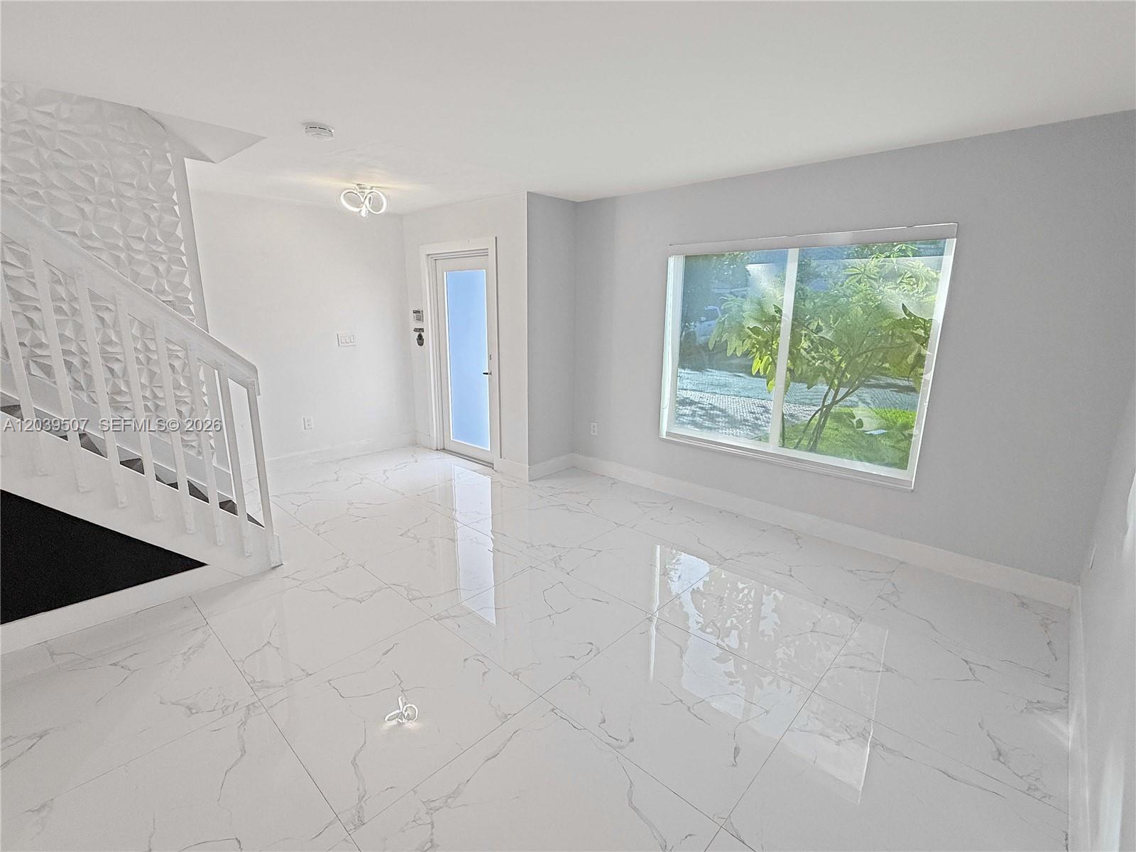 A bright room features white marble-look tile flooring, a staircase with textured wall panels, and a window — 16330 SW 102nd St, Miami FL 33196, MIAMI, FL