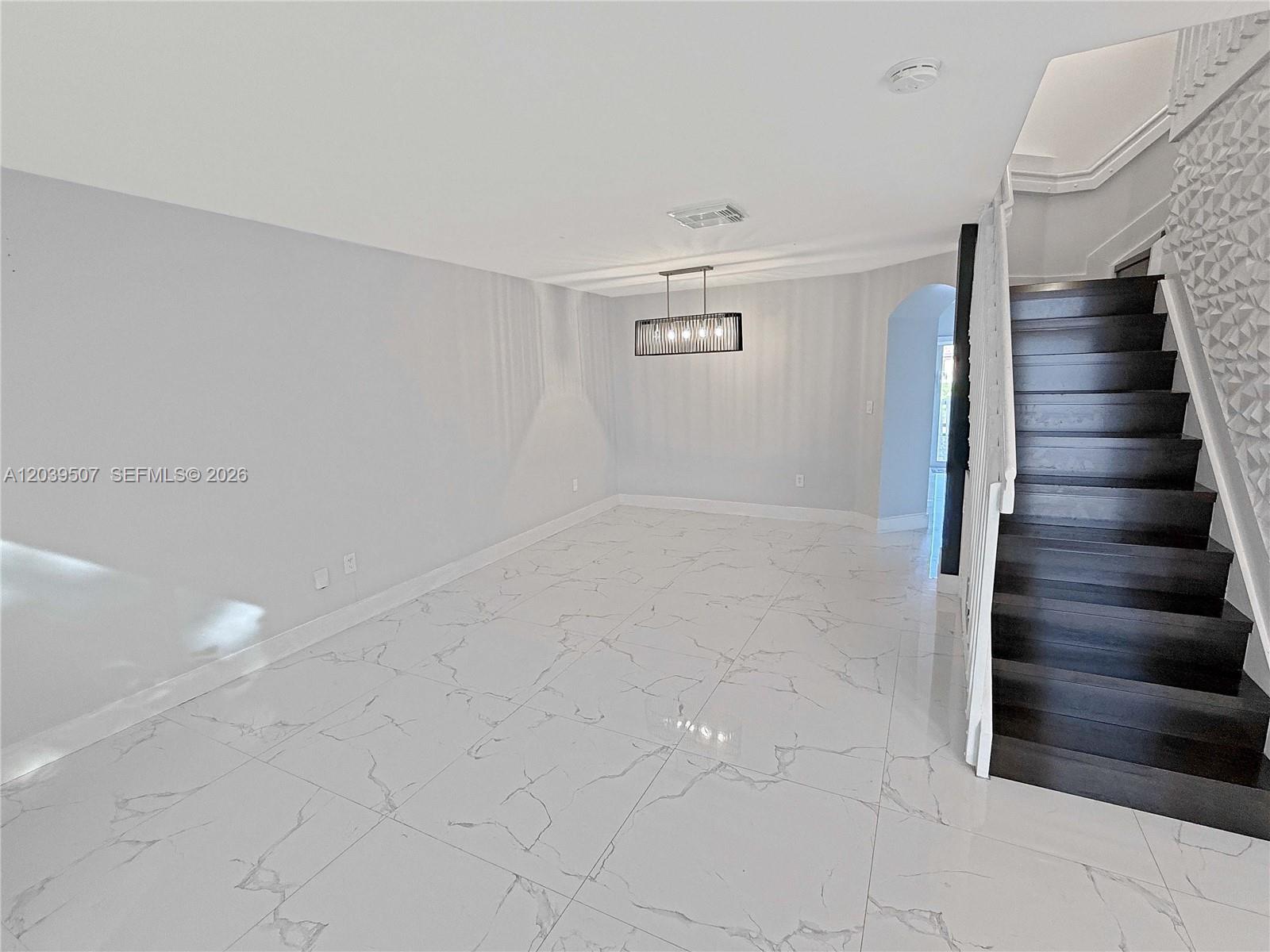 A dining room features white marble-look tile flooring, a modern rectangular chandelier, and dark stairs — 16330 SW 102nd St, Miami FL 33196, MIAMI, FL