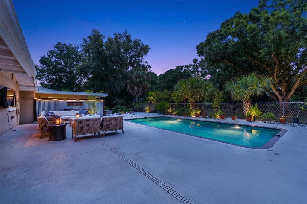 A backyard patio features a swimming pool, outdoor seating, and landscaping at dusk — 2515 49TH STREET, SARASOTA, FL
