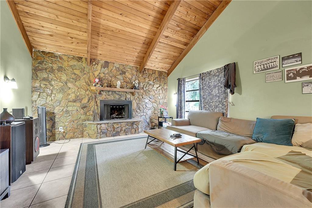 A living room features a stone fireplace, vaulted wood-paneled ceiling, tile floors, and a sectional — 7103 Arthurs Road, Fort Pierce FL 34951, FORT PIERCE, FL
