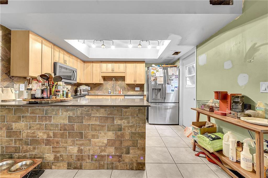 A kitchen features light wood cabinets, a stone-tiled island, stainless steel appliances, and tile flooring — 7103 Arthurs Road, Fort Pierce FL 34951, FORT PIERCE, FL
