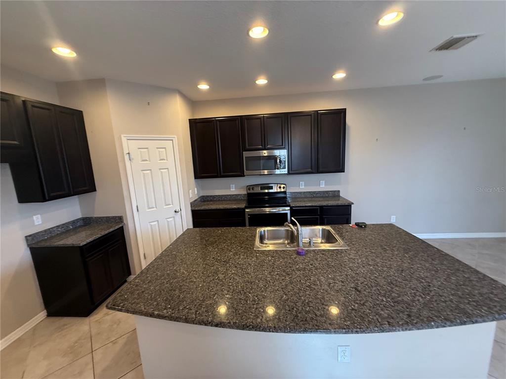 A kitchen features dark wood cabinets, granite countertops, a central island, and stainless steel appliances — 6629 HOLLY HEATH DRIVE, RIVERVIEW, FL