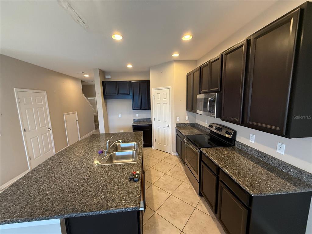 A kitchen features dark wood cabinets, granite countertops, a center island, and tile flooring — 6629 HOLLY HEATH DRIVE, RIVERVIEW, FL