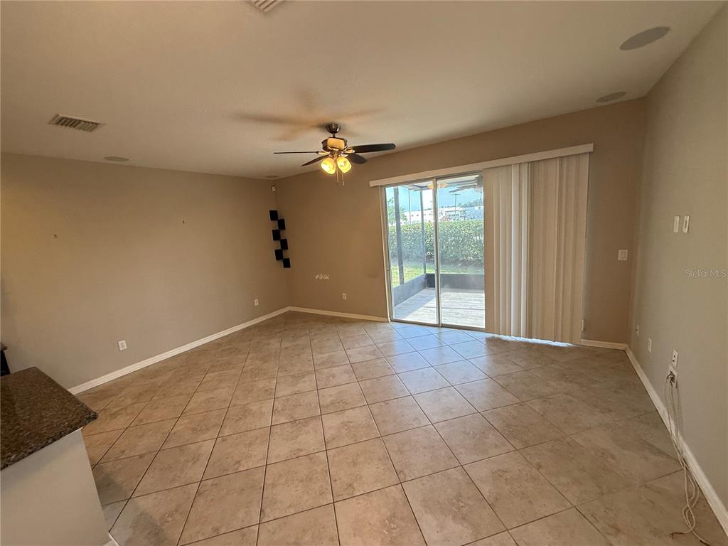 An empty living room features beige walls, tile flooring, a ceiling fan, and sliding glass doors — 6629 HOLLY HEATH DRIVE, RIVERVIEW, FL