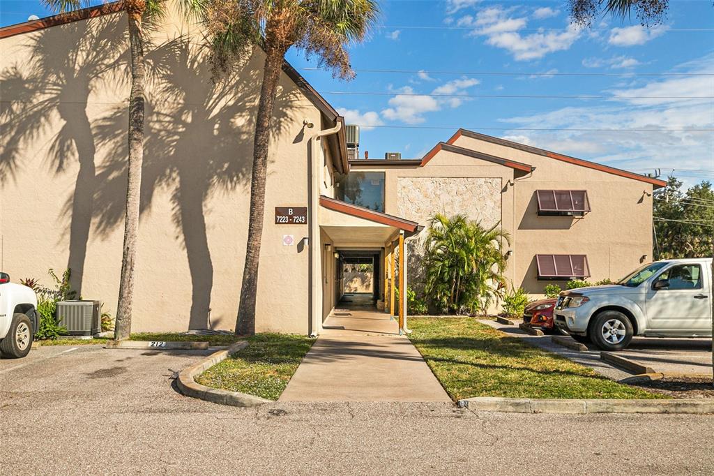 A two-story apartment building exterior features a covered walkway, palm trees, and parking spaces — 7223 CLOISTER DRIVE UNIT 111, SARASOTA, FL