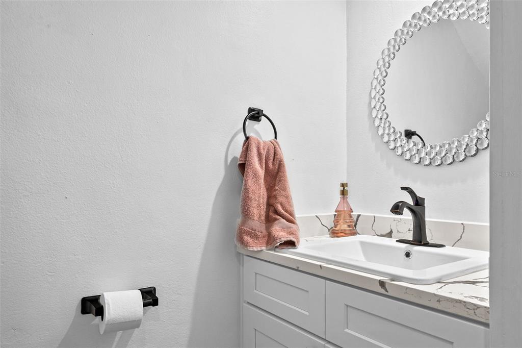 A bathroom features a white vanity with a marble countertop, a sink, and a round mirror — 7223 CLOISTER DRIVE UNIT 111, SARASOTA, FL