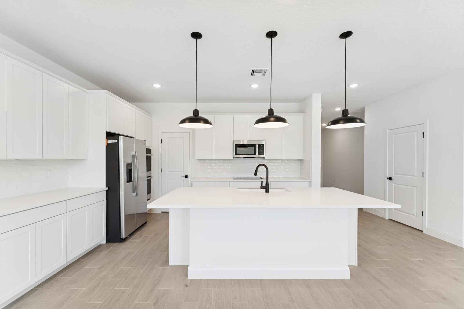 A modern kitchen features white cabinetry, a central island, stainless steel appliances, and pendant lighting — 200 SE Birch Terrace, Stuart FL 34997, STUART, FL