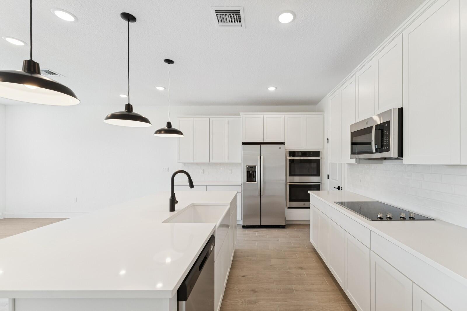A modern kitchen features white cabinetry, stainless steel appliances, a large island, and pendant lighting — 200 SE Birch Terrace, Stuart FL 34997, STUART, FL