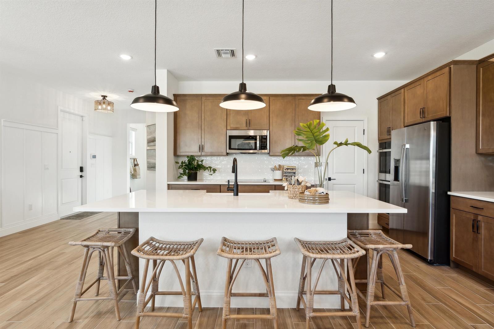A modern kitchen features a white island with five rattan stools and wooden cabinetry — 200 SE Birch Terrace, Stuart FL 34997, STUART, FL