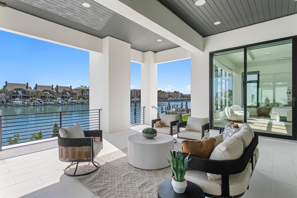 A covered outdoor patio features modern furniture, tile flooring, and a view of a marina — 500 BARCELONA DRIVE, TIERRA VERDE, FL