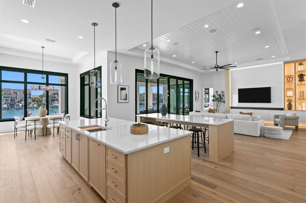 A modern open-concept kitchen and living area with light wood cabinets, quartz countertops, and waterfront views — 500 BARCELONA DRIVE, TIERRA VERDE, FL