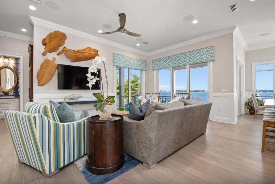 A living room features a striped armchair, a gray sofa, and large windows overlooking water — 110 10TH STREET S, BRADENTON BEACH, FL