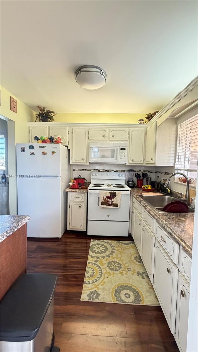 A kitchen features white cabinets, white appliances, dark wood flooring, and a patterned area rug — 5300 Washington St # D309, Hollywood FL 33021, HOLLYWOOD, FL