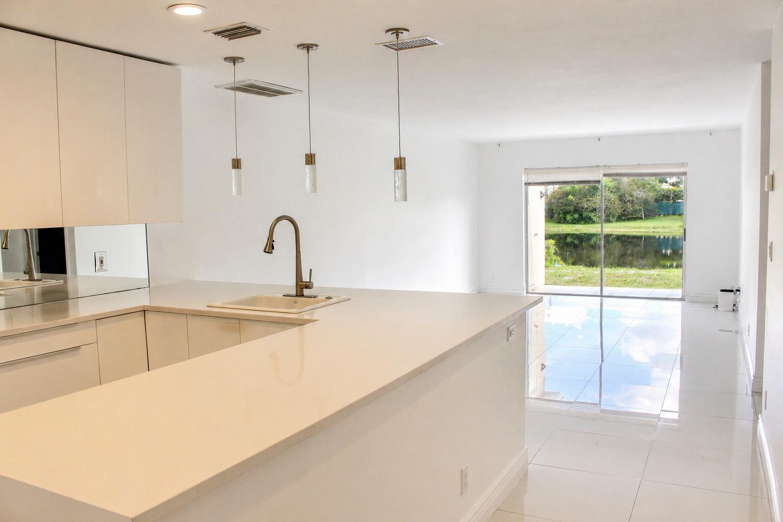 A modern white kitchen with a peninsula overlooks a living area and a backyard pond — 8861 Bella Vista Drive, Boca Raton FL 33433, BOCA RATON, FL
