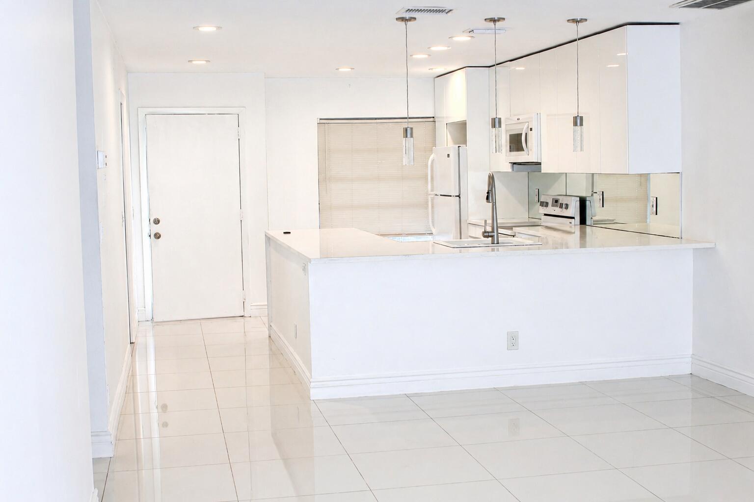 A modern white kitchen features glossy cabinets, a breakfast bar, and polished tile flooring — 8861 Bella Vista Drive, Boca Raton FL 33433, BOCA RATON, FL